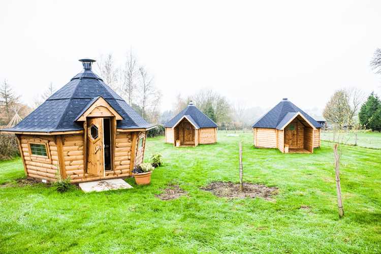 camping cabins yeaveley estate timber buildings in green field with trees in background with potted plants outside