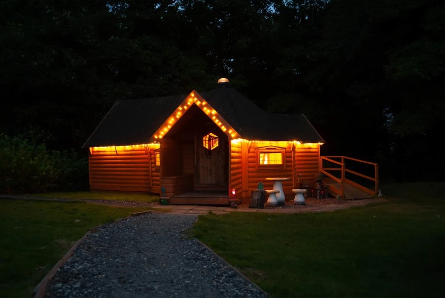 kits coty glamping camping cabin with fairy lights and toadstools out front